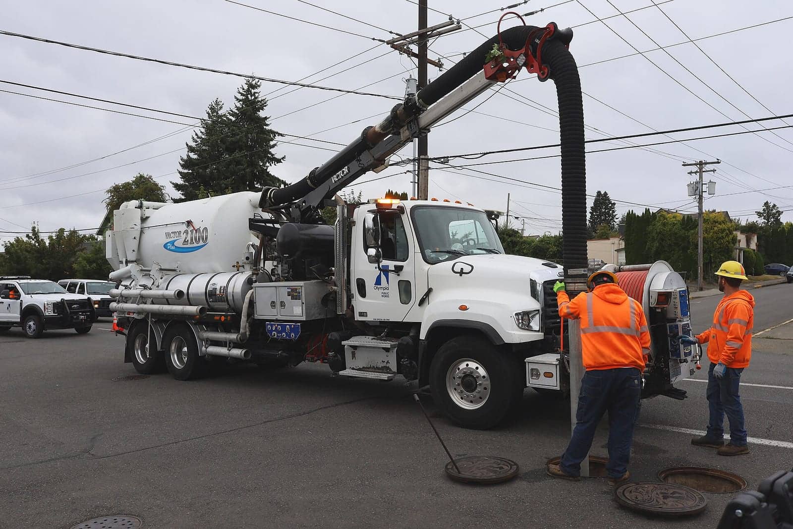 Full sewage vacuum truck operating a large suction hose on a U.S. street